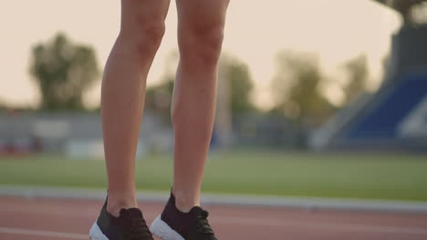 A-young-woman-athlete-brooding-warms-up-and-prepares-for-the-start-of-a-sprint-race-on-a-sunny-day-on-the-treadmill-of-the-stadium